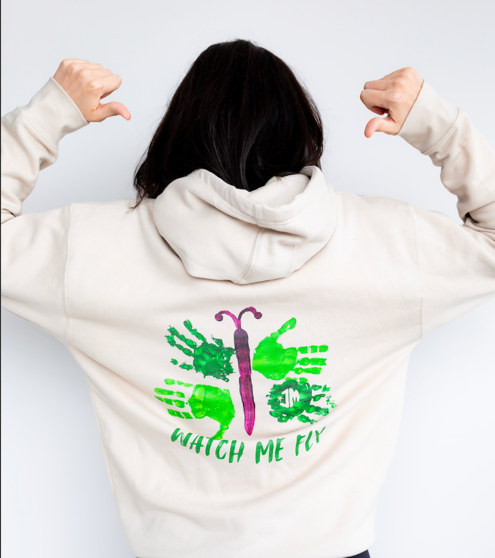 Female model wearing Hayden's "Watch Me Fly" hooding and pointing at the artwork on the back