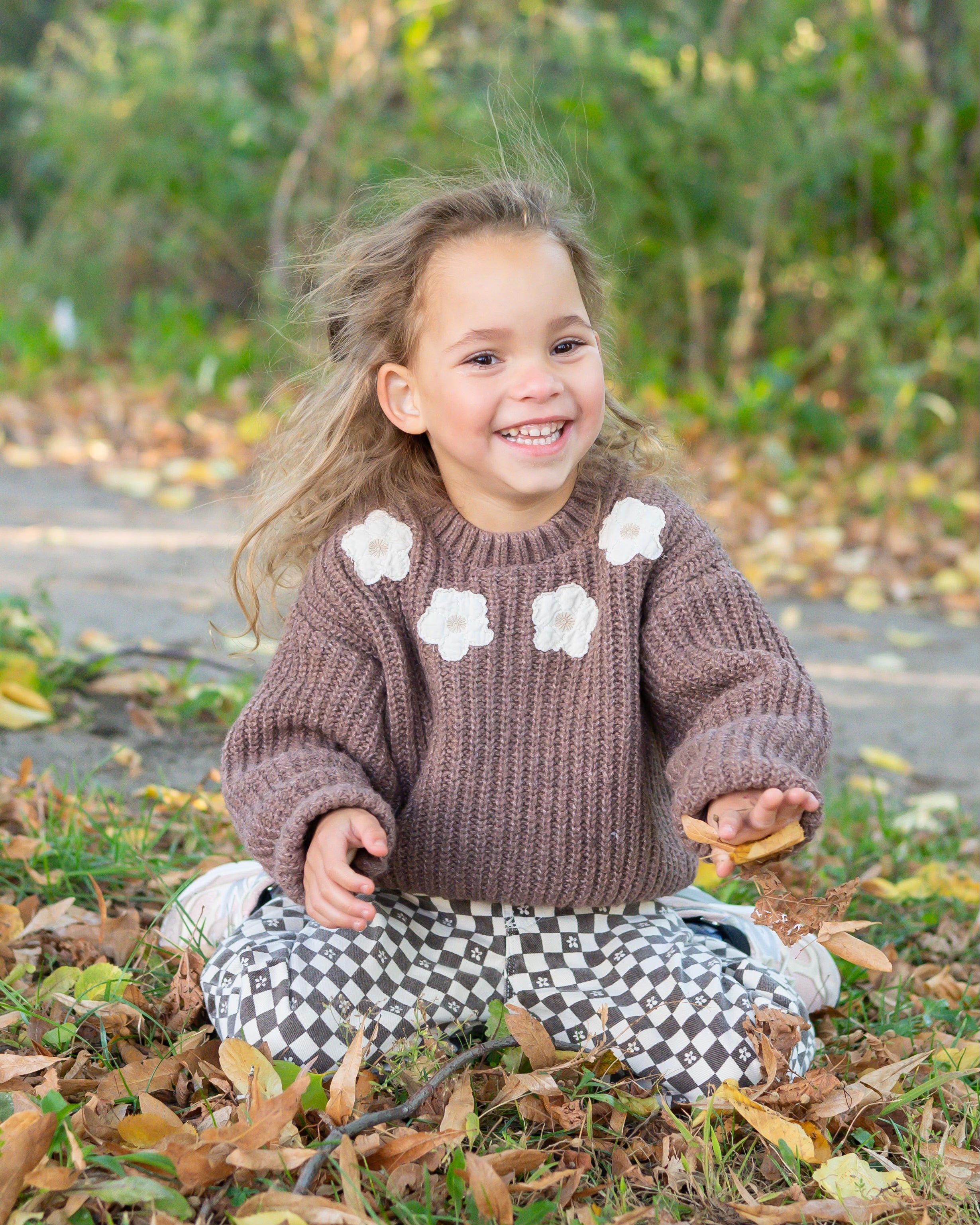 Maximizer Hayden sitting on the ground in leaves and smiling wearing a brown sweater with flowers