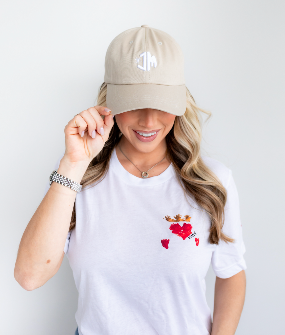 Female model wearing Maximizer Kitty's "Queen of Hearts" white shirt and a JM logo hat